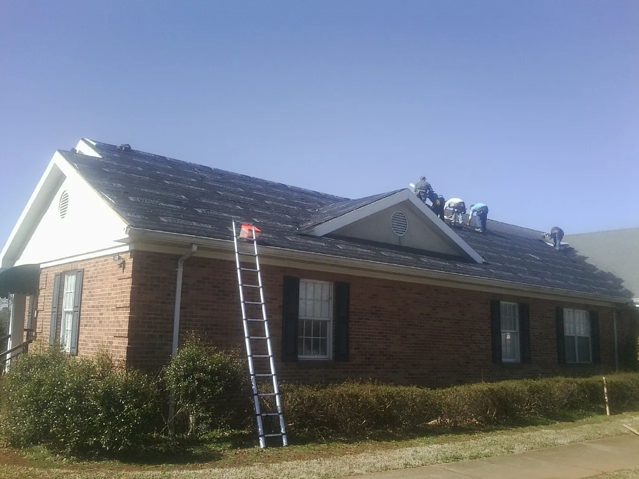 Crew tearing shingles off a brick ranch roof with a ladder set — Metal Roof Repair work by our crew in Friendsville