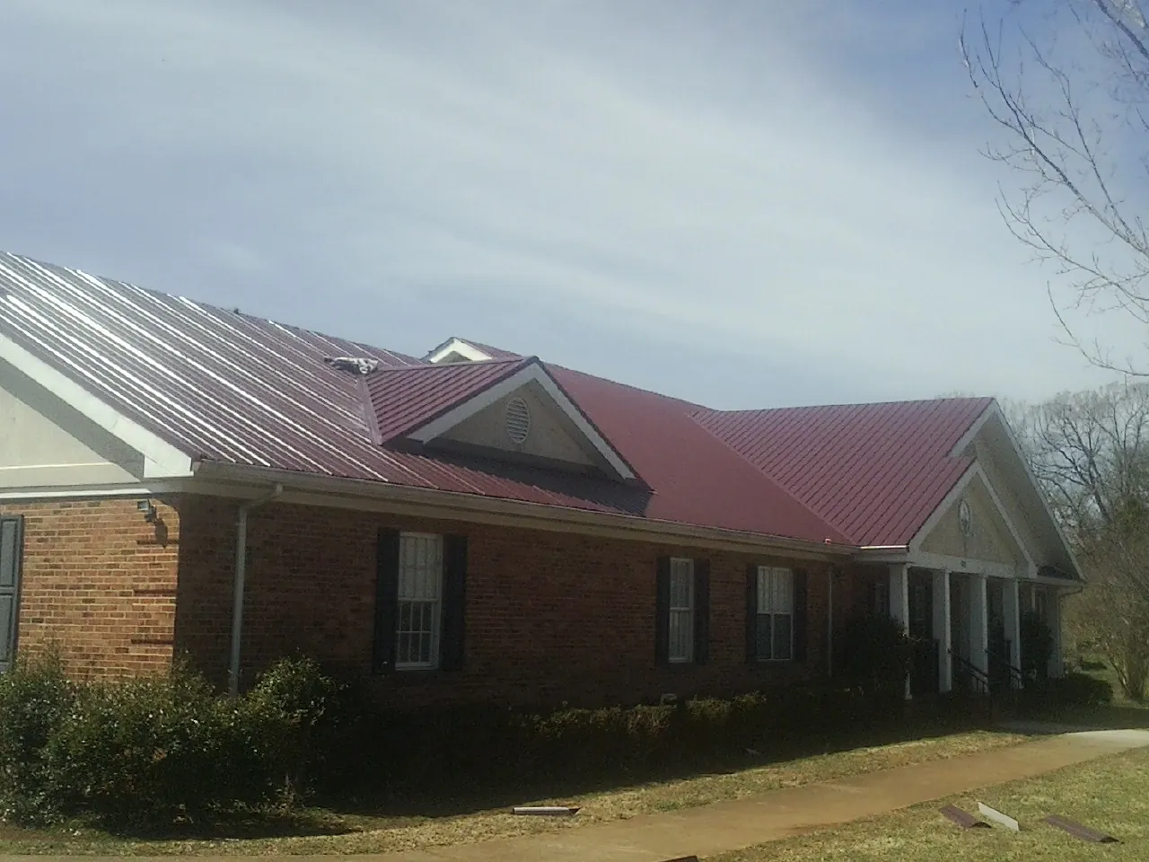 Red metal roof with gabled entries on a long brick building, from a Hail Damage Roof Repair job in Friendsville