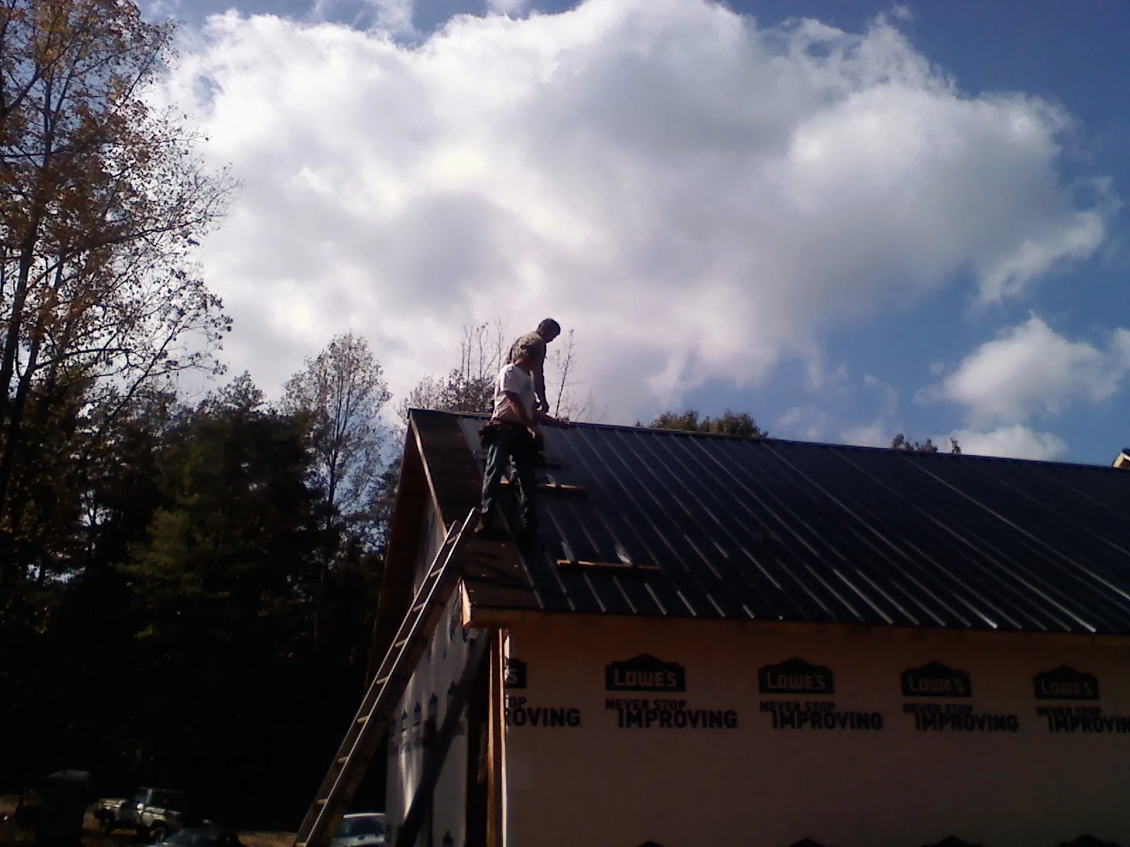 Roofer fastening dark metal panels high against a cloudy sky, from a Roof Inspection job in Friendsville