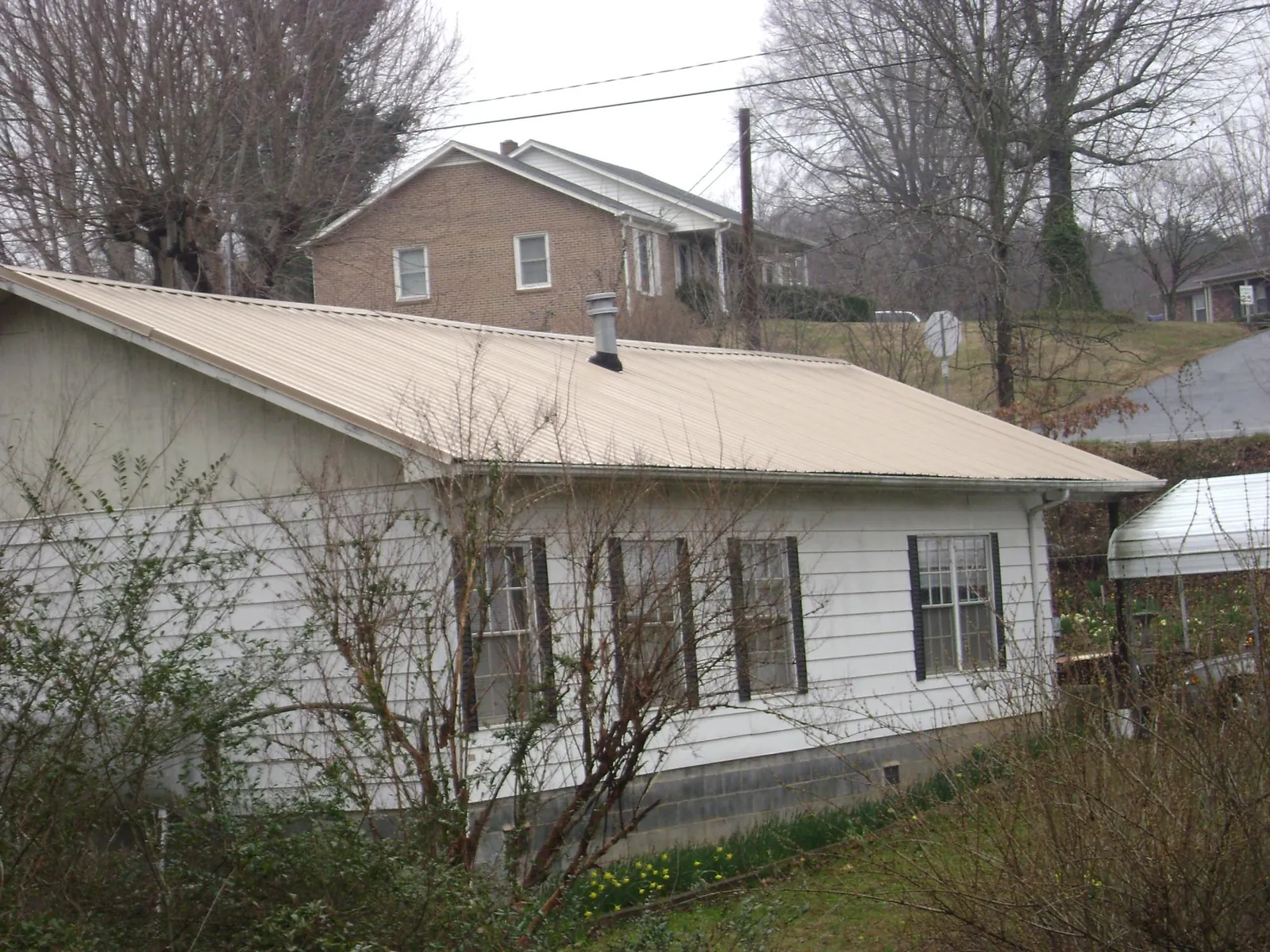 Tan metal roof on a white sided house set into a hillside — Commercial Roofing by Roofing Brothers in Friendsville