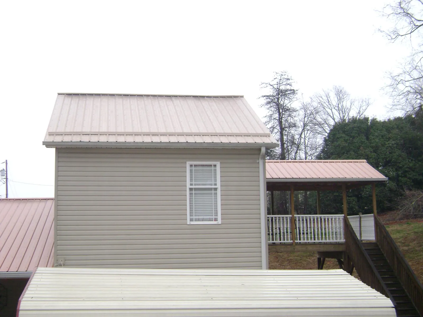 Tan metal roofs on a two story addition and attached porch, from a Roof Replacement job in Friendsville